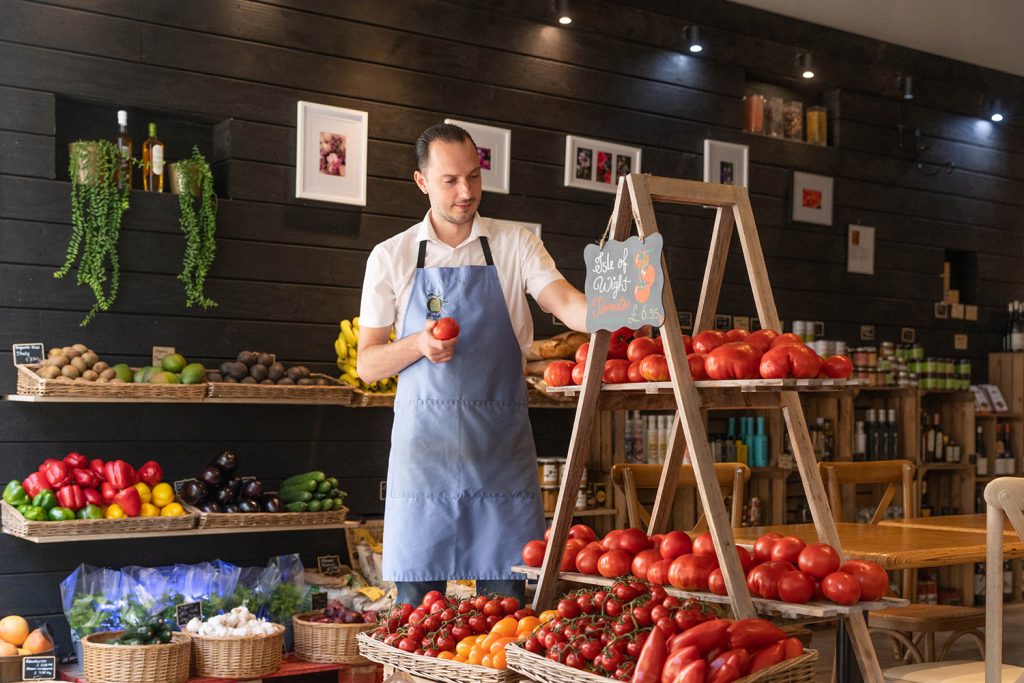 A man in an apron is standing in front of a display of vegetables.